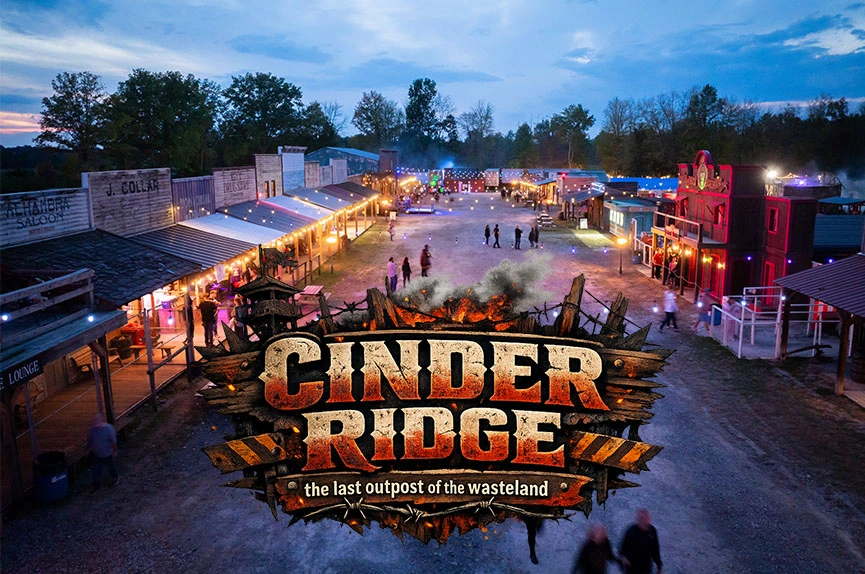 cinder-ridge-town A wide night shot of an old-western style ghost town street lined with rustic wooden storefronts and illuminated by warm string lights, with patrons walking through the area. The text reads "Cinder Ridge the last outpost of the wasteland"