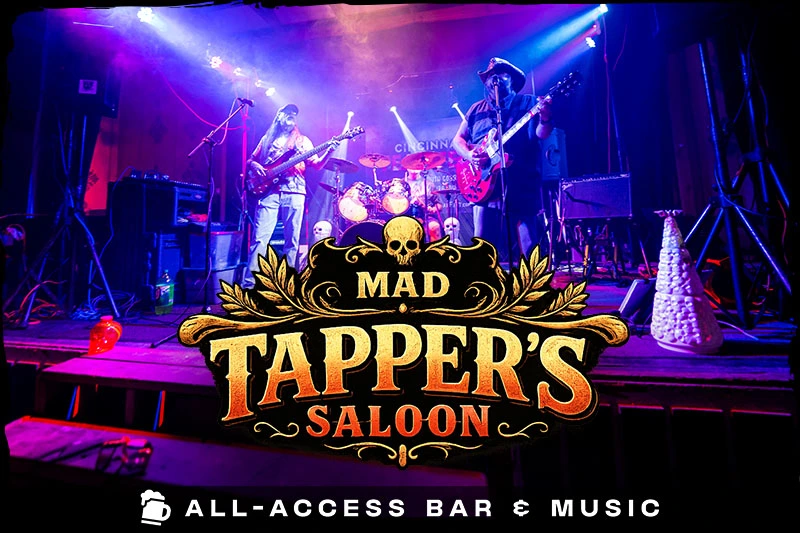 mad-tappers-saloon (1) A live rock band performs on a stage bathed in vibrant blue and purple concert lighting, with decorative skulls lining the front edge. The text reads "Mad Tapper's Saloon. All-Access Bar & Music."